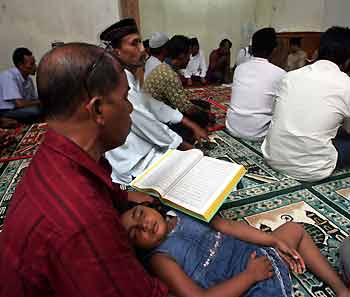 An Acehnese child sleeps as her father reads the Koran during a memorial service for last year's Indian Ocean tsunami victims in the district of Landung in Banda Aceh December 25, 2005. 
