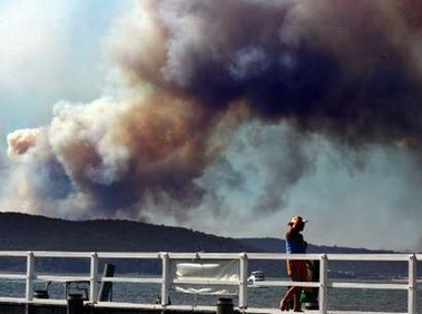 A woman walks along a wharf in the northern Sydney suburb of Palm Beach as smoke from a fire on the Central Coast can be seen in the sky behind January 1, 2006. 