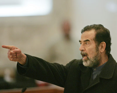 Former Iraqi leader Saddam Hussein gestures during his trial in Baghdad February 13, 2006. Saddam returned to court on Monday and immediately launched into tirades, pounding the railing of his metal pen, condemning the court and saying he had been forced to attend the trial, a Reuters witness said. [Reuters]