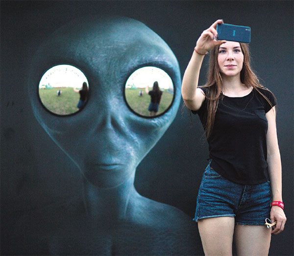 A Woman Photographs Herself In Front Of An Image Of An Alien With Mirrored Eyes At The Alfa