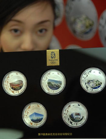 A saleswoman shows a set of commemorative badges featuring five of the venues for the Beijing Olympic Games: (from top left to bottom right ) the National Stadium, or 'Bird's Nest', Qingdao Olympic Sailing Center, Hong Kong Olympic Equestrian Venue, National Aquatics Center, or 'Water Cube', and Shenyang Olympic Stadium , in Beijing, March 16, 2008. [Xinhua]