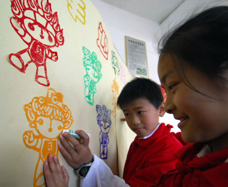 Two students use glue to stick a paper-cut Fuwa of Bei Beithe Fish, a mascot for the Beijing Olympic Games, on a classroom wall in a Nanchang primary school in East China&apos;s Jiangxi Province, March 31, 2008. The school encouraged students to make Fuwa-themed paper-cuts to celebrate the upcoming Olympics. [Xinhua]