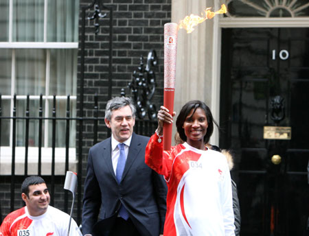 British Prime Minister Gordon Brown (C) stands with athlete Denise Lewis carrying the Olympic torch as physically challenged athlete Ali Jawade (L) waits for relay outside 10 Downing Street in London April 6, 2008. The Beijing Olympic torch relay proceeds in London, which will be the largest city relay outside the Chinese mainland. [Xinhua]