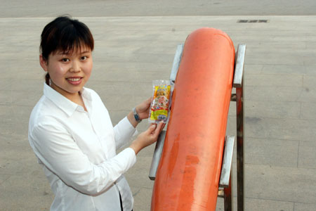 A Chinese worker compares a small bag of sausage to a bigger one produced by a company in Zhucheng, East China's Shandong Province, June 7, 2006. The bigger sausage is two meters long and weighs 90 kilograms. The company will apply for the Guinness World Records for the sausage. [newsphoto]
