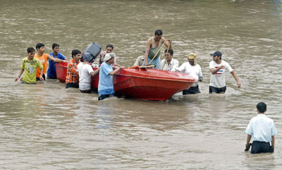 People move through a flooded road in Surat, about 260 km (162 miles) south of the western Indian city of Ahmedabad, August 8, 2006. Swirling floodwaters inundated several towns and cities in western and southern India on Tuesday as the military deployed helicopters and boats to help hundreds of thousands of marooned people. 