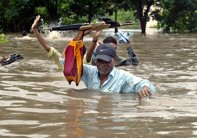 People move through a flooded road in Surat, about 260 km (162 miles) south of the western Indian city of Ahmedabad, August 8, 2006. Swirling floodwaters inundated several towns and cities in western and southern India on Tuesday as the military deployed helicopters and boats to help hundreds of thousands of marooned people. 