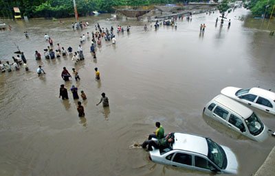 People move through a flooded road in Surat, about 260 km (162 miles) south of the western Indian city of Ahmedabad, August 8, 2006. Swirling floodwaters inundated several towns and cities in western and southern India on Tuesday as the military deployed helicopters and boats to help hundreds of thousands of marooned people. 