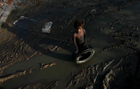 A boy looks at the camera as he holds a tyre at a demolished slum colony in New Delhi September 10, 2006. 