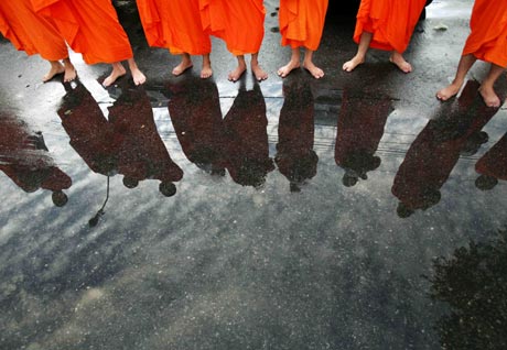 Thai Buddhist monks are reflected on wet pavement as they wait to collect alms outside a temple near the Government House in Bangkok September 22, 2006. 