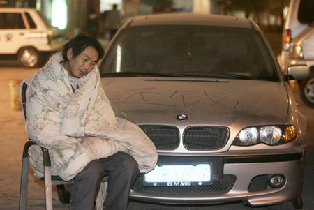 Zhou Gongwen, a migrant worker, rests near a BMW at a police station in Chongqing, December 5, 2006. Zhong and some thirty other migrant workers completed a project for a man surnamed Liu in 2003 but hadn't received payment. On December 1, 2006, Zhong and other migrant workers found Liu, and called the police to seize Liu's car. The migrant workers took turns watching the car to prevent it from being driven away. The Chinese characters on the car read
