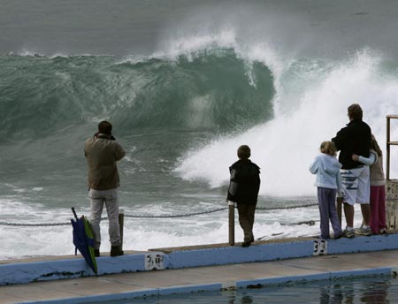 Onlookers watch a wave break at Dee Why Point in Sydney June 10, 2007. The death toll from a storm and torrential rain hitting Australia's east coast stands at seven with two still missing, said police as forecasters say conditions will begin to ease. 