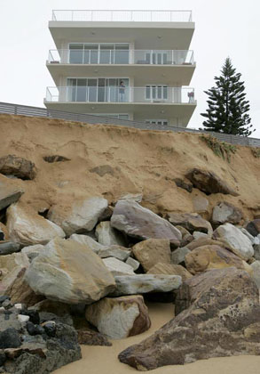 A resident of a water's edge apartment block stands on his balcony above rocks exposed by high seas at South Narrabeen Beach in Sydney June 10, 2007. The death toll from a storm and torrential rain hitting Australia's east coast stands at seven with two still missing, said police as forecasters say conditions will begin to ease. 
