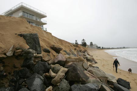 A man walks his dog past rocks exposed by high seas near an apartment block at South Narrabeen Beach in Sydney June 10, 2007. The death toll from a storm and torrential rain hitting Australia's east coast stands at seven with two still missing, said police as forecasters say conditions will begin to ease.