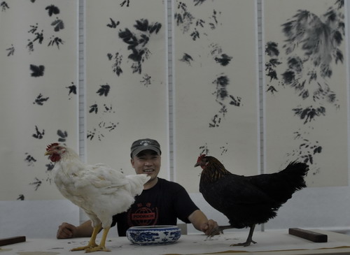 Chinese painter Xiao Hu watches as two chickens walk on a paper at a studio in Songzhuang, Beijing, July 21, 2007. Xiao Hu bought the two chickens at a market, painted their claws with ink, and then let the chickens to walk on the white paper, making a painting. [Pan Songgang/China Population News]