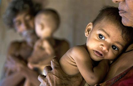 A tribal woman (R) holds her granddaughter Rohini as her grandson Rohit is carried by her husband inside a hut in Mumbai July 25, 2007. The seven-month-old twins Rohini and her brother Rohit from a tribal family have been declared malnourished by a team of the city's civic administration doctors, local media reported. India, home to millions of underfed children despite its flourishing economy, will have eradicated malnutrition by 2015, the country's health minister said. A government survey released this year however found that 46 percent of children under the age of three years were undernourished.