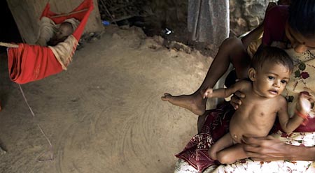 A tribal woman holds her daughter Rohini as her son Rohit sleeps in a hammock inside a hut in Mumbai July 25, 2007. The seven-month-old twins Rohini and Rohit have been declared malnourished by a team of the city's civic administration doctors, local media reported. India, home to millions of underfed children despite its flourishing economy, will have eradicated malnutrition by 2015, the country's health minister said. A government survey released this year however found that 46 percent of children under the age of three years were undernourished.