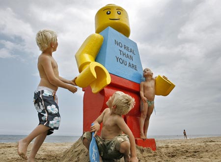 Children play near a giant smiling Lego man that was fished out of the sea in the Dutch resort of Zandvoort August 7, 2007. Workers at a drinks stall rescued the 2.5-metre (8-foot) tall model with a yellow head and blue torso. The toy was later placed in front of the drinks stall. 