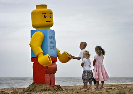 Children play near a giant smiling Lego man that was fished out of the sea in the Dutch resort of Zandvoort August 7, 2007. Workers at a drinks stall rescued the 2.5-metre (8-foot) tall model with a yellow head and blue torso. The toy was later placed in front of the drinks stall. 