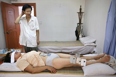 A doctor stands by a patient who is receiving a special acupuncture treatment at Huangzhiguo Traditional Chinese Massage and Acupuncture Clinic in Shanghai August 8, 2007. Chinese acupuncture and moxibustion are based on the traditional Chinese medicine theory that heat from burning moxa transmitted to the skin indirectly through needles can help relieve pains on the waist, neck, or shoulder. 