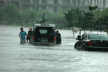 People try to push a car stranded through a flooded street after heavy rains in Yantai, East China’s Shandong Province, August 10, 2007. [Xinhua]