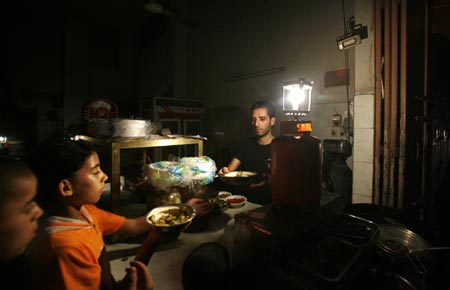 A Palestinian vendor works by the light of a gas lamp in his shop during a power cut in Gaza August 20, 2007.