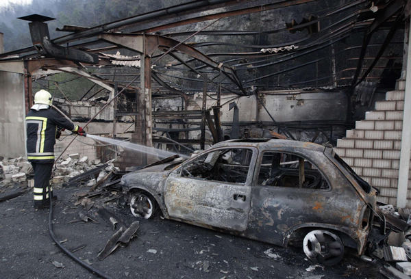 A fireman sprays water in a burned car body repair workshop beside a destroyed car next to the southwestern village of Visp April 26, 2011. On Tuesday afternoon a fire erupted in the body repair workshop and later spread to the nearby forest, local police reported. Switzerland village sees forest fire