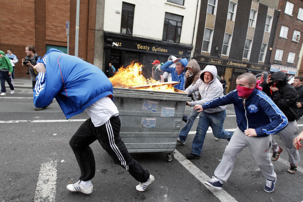Youths push a burning rubbish bin towards riot police during a demonstration in north Dublin May 17, 2011. Britain's Queen Elizabeth begins a four day state visit to Ireland today which is the first state visit by a British monarch since Ireland's independence. Queen's visit to Ireland prompts violent clashes