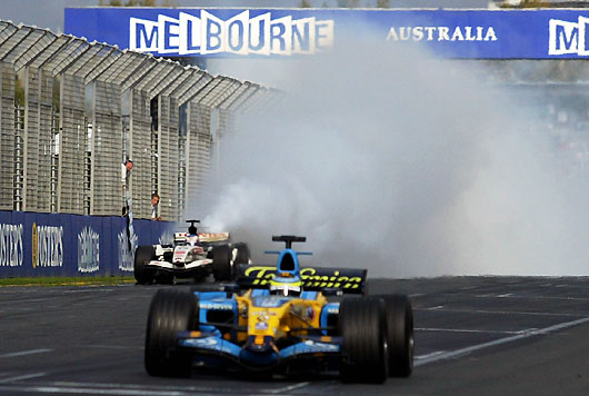 Renault Formula One driver Giancarlo Fisichella of Italy crosses the finish line as Honda's Jenson Button of Britain's car belches smoke