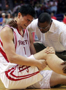 Houston Rockets center Yao Ming (L) grimaces as Rockets trainer Keith Jones checks his injury in the first half of their NBA game against the San Antonio Spurs in Houston, Texas, March 18, 2006. [Reuters]