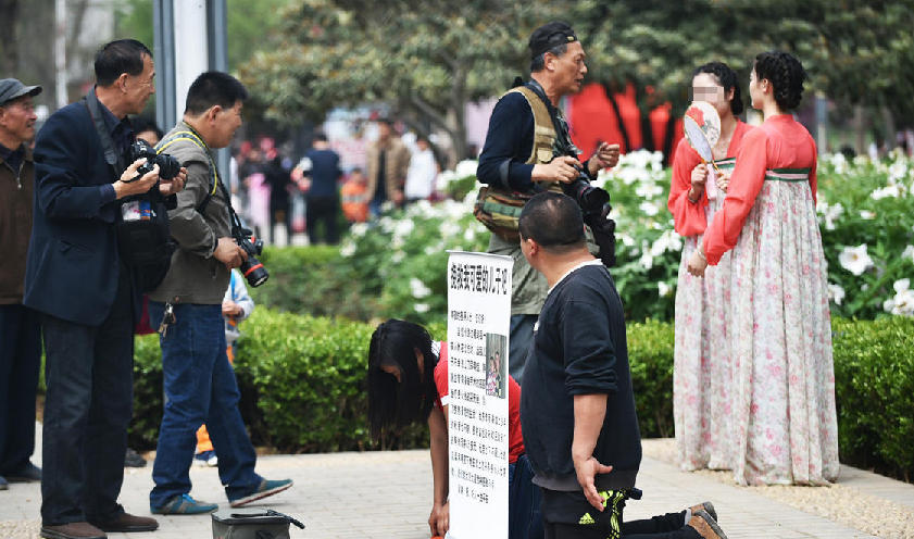 一边是夫妇跪地乞讨 一边是美女羞笑拍照