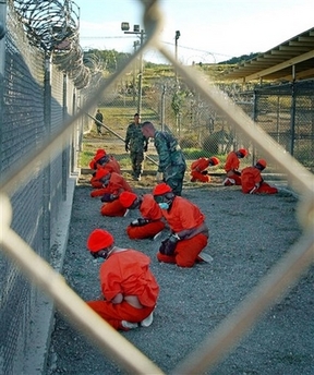 In this Jan. 11, 2002 file photo released by the U.S. Navy, detainees in orange jump suits sit in a holding area under the watchful eyes of military police at Camp X-Ray at Naval Base Guantanamo Bay, Cuba, during in-processing to the temporary detention facility. In the few short years since the first shackled Afghan shuffled off to Guantanamo, the U.S. military has created a global network of overseas prisons, its islands of high security keeping 14,000 detainees beyond the reach of established law. (AP