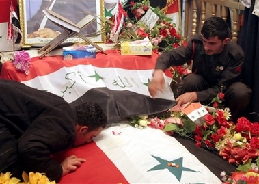 A man kisses the grave of the executed former Iraqi leader Saddam Hussein while another man wearing a uniform of the former Republican Guard, an army unit that used to serve as the presidential bodyguard adjusts an Iraqi flag in Ouja, 115 kilometers (70 miles) north of Baghdad, Iraq, Sunday, Jan. 7, 2007. An unauthorized video of Saddam's execution, showing him being taunted on the gallows and his body dangling at the end of a rope, has ignited protests by Saddam's fellow Sunni Arabs in several Iraqi cities. (AP