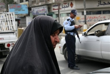 woman passes by a vehicle checkpoint as an Iraqi policeman checks the identity of a driver in Baghdad, Iraq, Thursday, March 8, 2007.