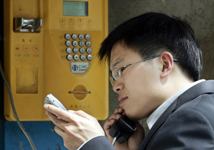 A man chats on a public telephone while checking his mobile phone in Beijing April 24, 2006. 