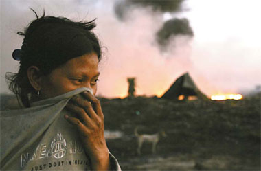 A woman covers her face as she burns tires at a garbage dump at sunrise in order to recover the scrap metal inside to sell in Malabon, Metro Manila, on Friday. REUTERS