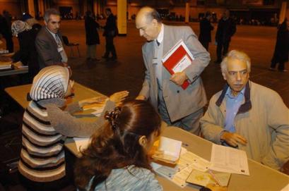 Iraqi election officials, seated at left and standing, at a registration desk for the Iraq expatriates at Wembley Conference Centre in north-west London, Monday, Jan. 17, 2005. Iraqi expatriates can register at the center to vote in the forthcoming election in Iraq for an Assembly that will draft a constitution and choose a president. Eligible Iraqis abroad, estimated to number 1.2 million, can vote in 14 countries: Britain, Australia, Sweden, Canada, Denmark, France, Germany, Iran, Jordan, the Netherlands, Syria, Turkey, United Arab Emirates and the United States. The man seated at right is registering. [AP]