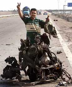 An Iraqi youth flashes a victory sign near the charred remains of one of two suicide car bombs, which were followed by clashes in Abu Ghraib, west of Baghdad, April 3, 2005. Al Qaeda's wing in Iraq claimed responsibility for a brazen overnight raid on Abu Ghraib prison that wounded 44 U.S. soldiers, according to an Internet statement, and said more attacks would follow. 