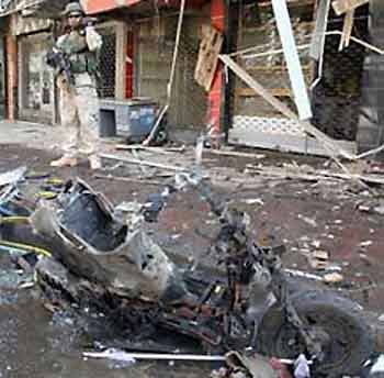 A U.S. soldier stands near a destroyed motorcycle used as a bomb in the northern city of Mosul June 2, 2005.