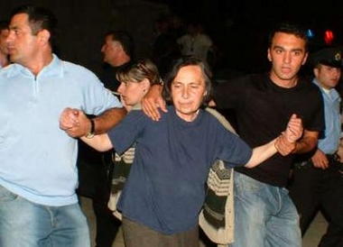 Georgian policemen lead the mother of the man suspected of throwing a grenade during a speech by visiting U.S. President George W. Bush in May, in Tbilisi, July 20, 2005. 