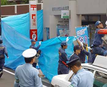 Japanese police officers investigate as they cover the crime scene with a blue sheet at a post office in Fukuoka, southern Japan July 25, 2005. A small package exploded at the post office on Monday but there were no injuries, police said.