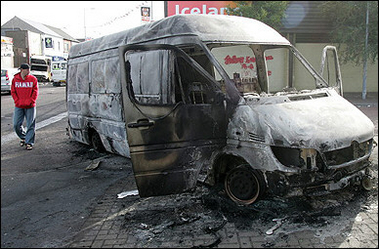 A man walks by the charred remains of a van on the footpath on the Shankill Road area of west Belfast 11 September 2005.