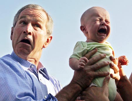 U.S. President George W. Bush hands back a crying baby that was handed to him from the crowd as he arrived for an outdoor dinner with German Chancellor Angela Merkel in Trinwillershagen, Germany, July 13, 2006.