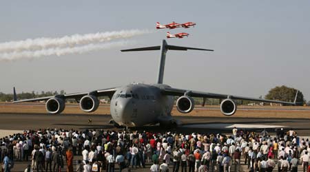 Pilots from the Indian Air Force Surya-Kiran aerobatic team fly over a U.S. C-17 military aircraft during the