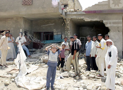 Iraqis stand outside a house damaged by a rocket attack in Baghdad May 6, 2006. Two children ages 5 and 6 were killed and three adult civilians were wounded when a mortar round landed on Baghdad's western district of Shula on Saturday, police said. 